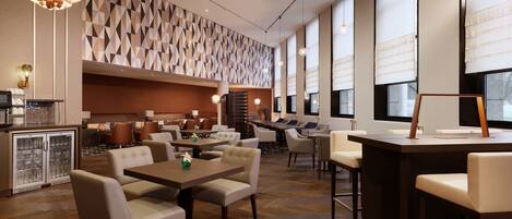 Un restaurante moderno con techos altos, patrones geométricos en las paredes y diferentes opciones de asientos, incluyendo cabinas y mesas.