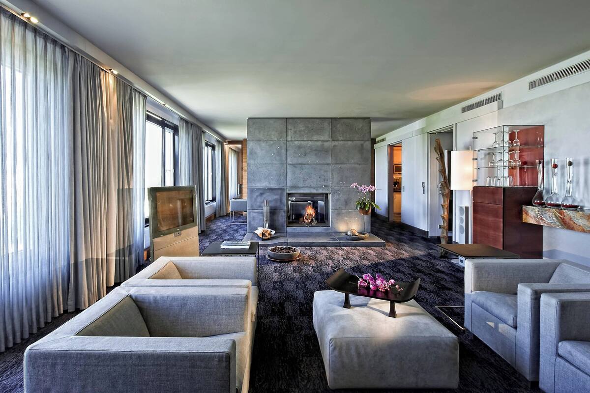 Une chambre d’hôtel moderne dotée d’une cheminée, de sièges confortables et d’une grande fenêtre avec des rideaux.