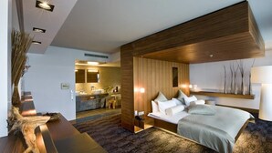 Une chambre d’hôtel moderne dotée d’un grand lit, d’un mur décoratif en bois, d’un bureau intégré et d’une salle de bain visible à travers une porte ouverte.