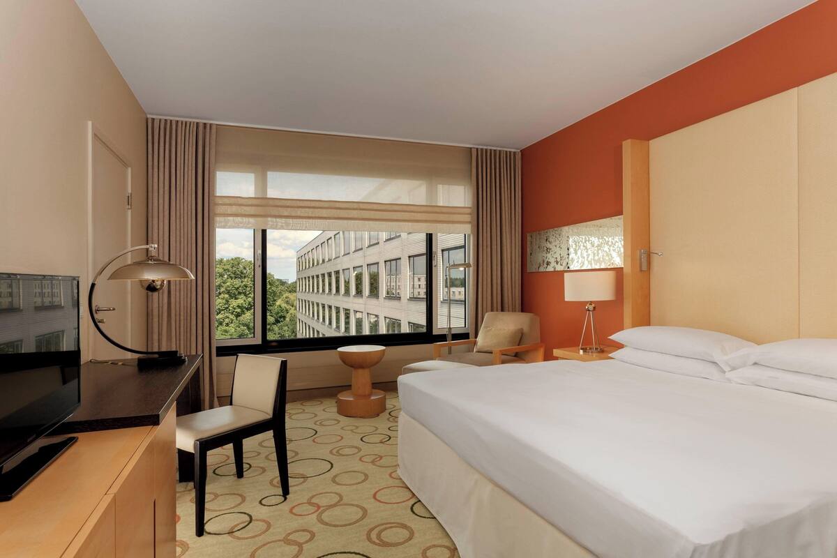 Une chambre d’hôtel avec un lit, un bureau, une chaise et une vue sur un immeuble par la fenêtre.