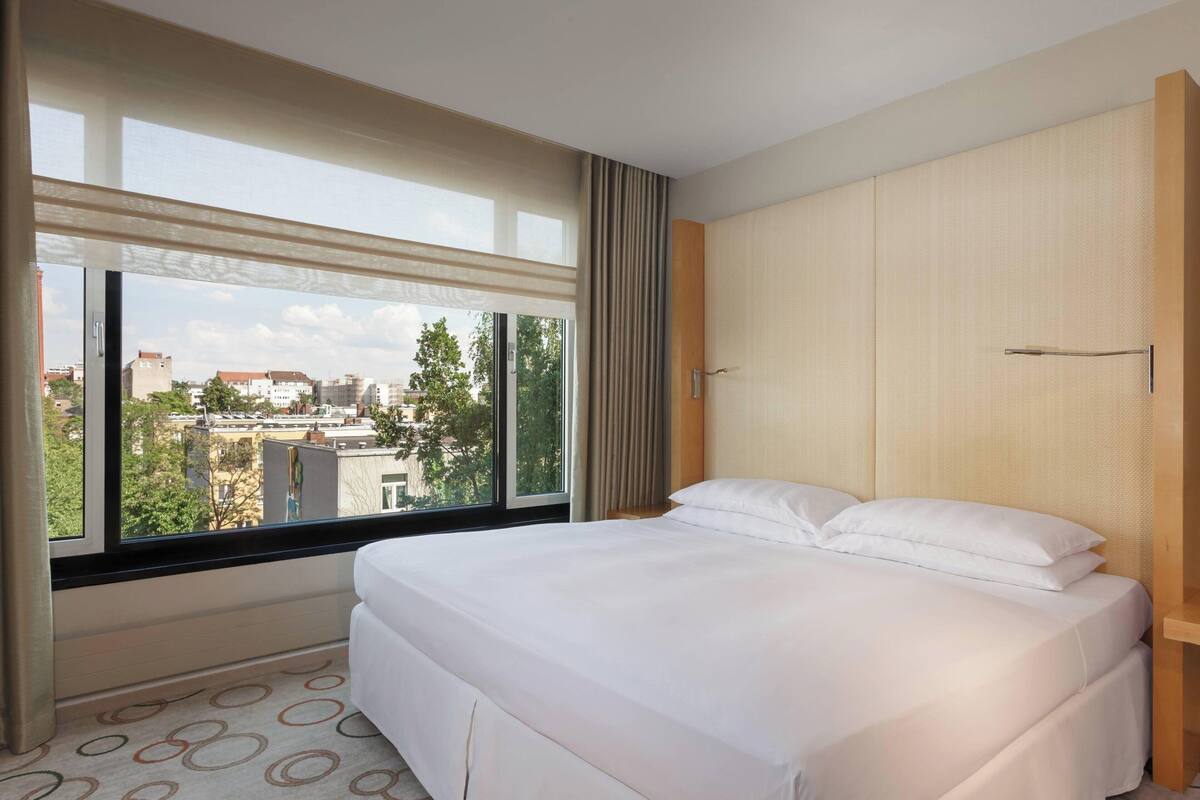 Une chambre d’hôtel avec un grand lit, une fenêtre avec des rideaux et une vue sur les bâtiments environnants.
