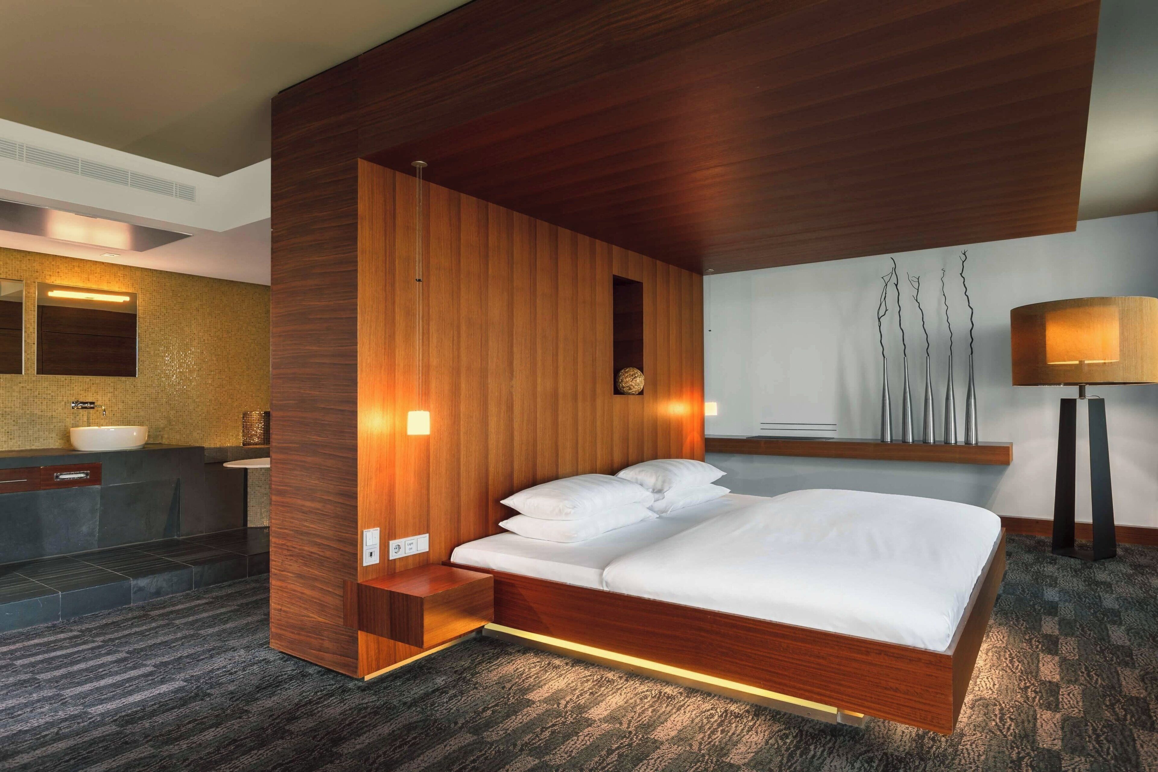 Une chambre d’hôtel moderne avec un mur d’accent en bois, un grand lit, un lavabo intégré et un miroir au-dessus du lavabo.