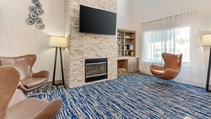 A modern living room with a stone fireplace, a flat-screen TV, and two leather chairs.