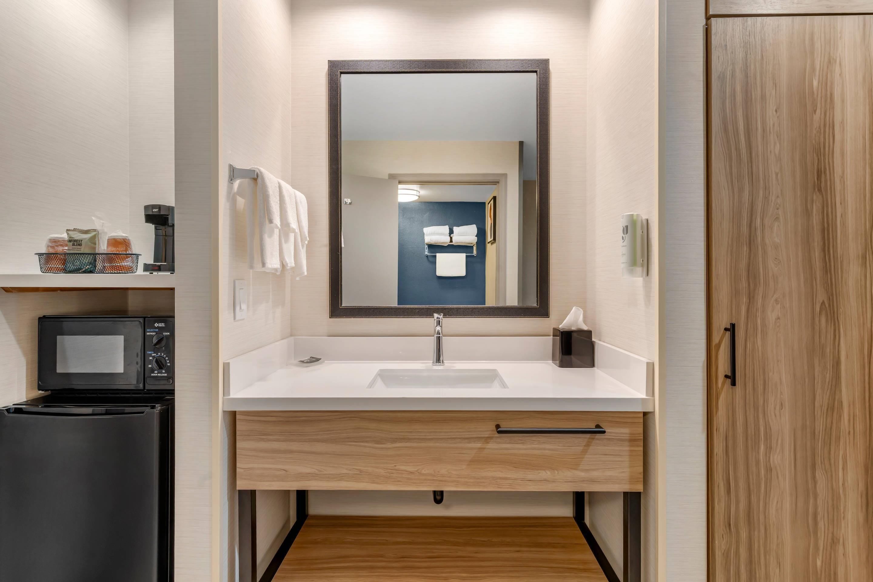 Un baño moderno con un lavabo blanco, un espejo, un perchero y un microondas.