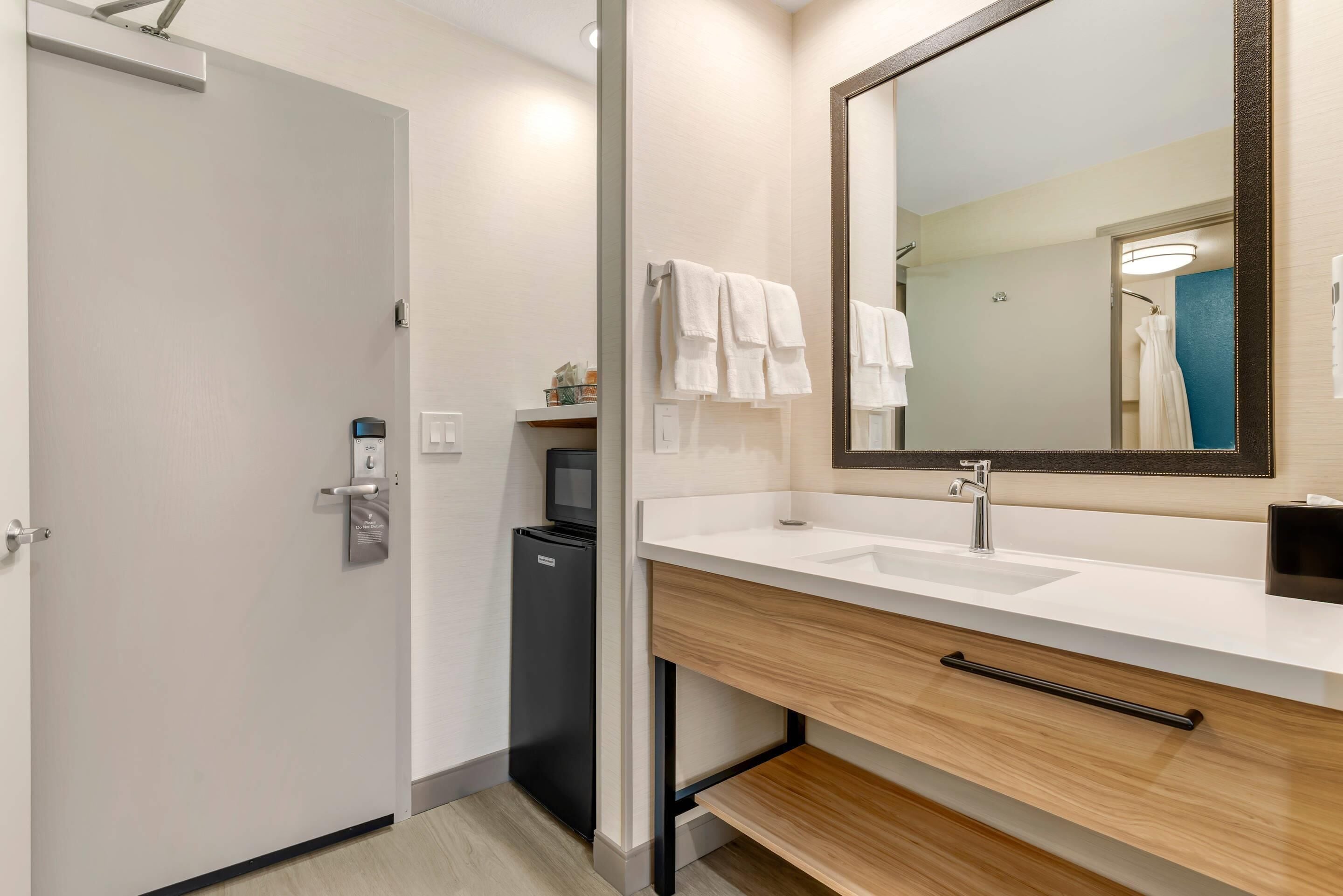 A modern bathroom with a white sink, a large mirror, and a black refrigerator.
