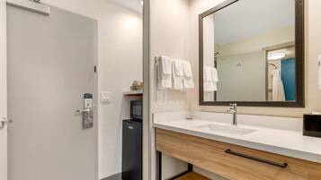 A modern bathroom with a white sink, a large mirror, and a black refrigerator.