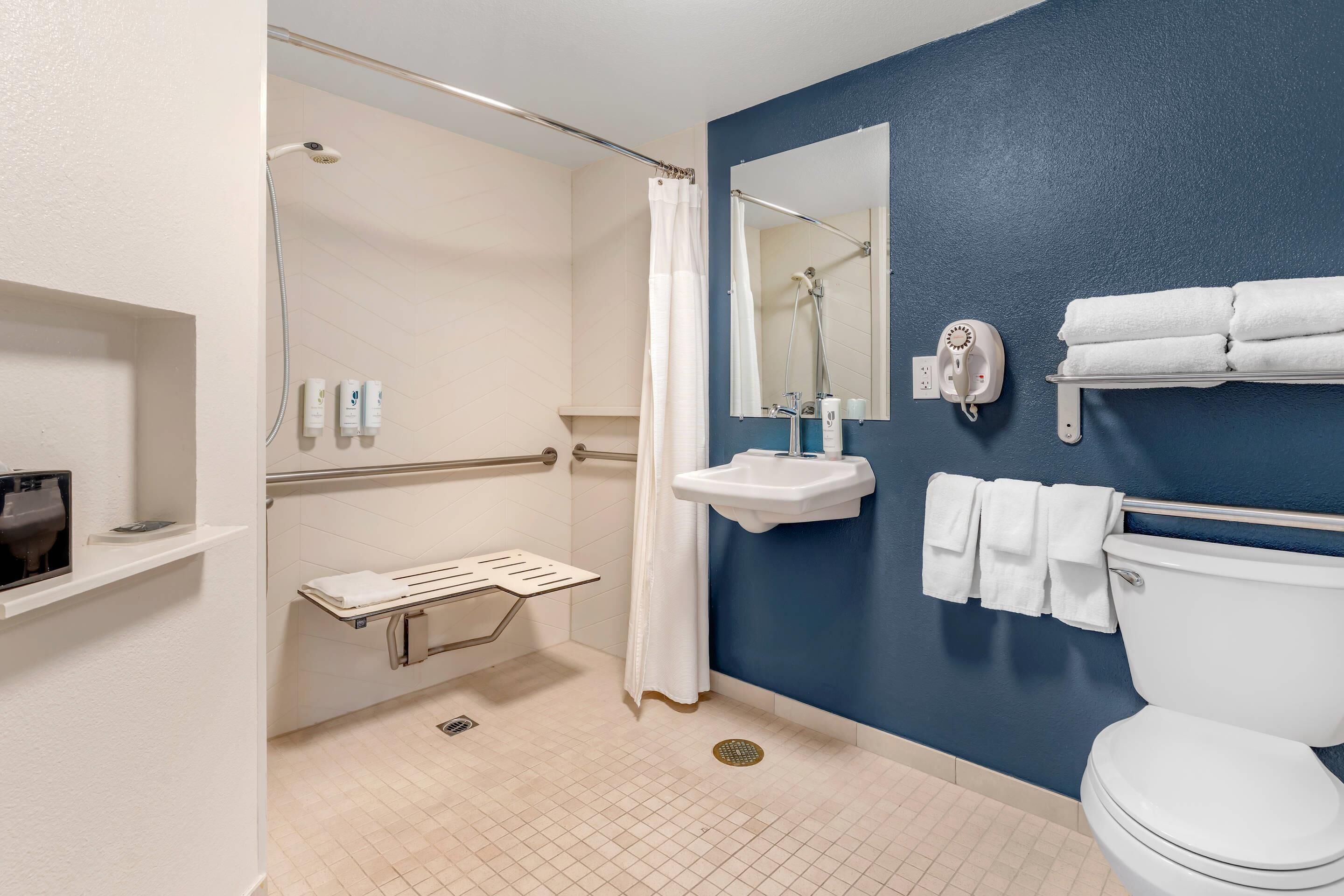 A bathroom with a shower, toilet, sink, and hand dryer.