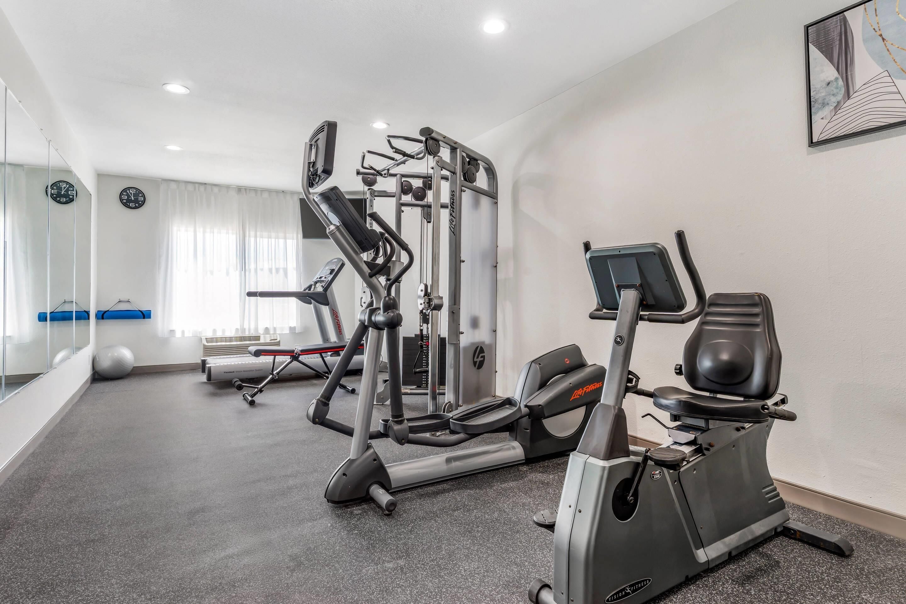 Un gimnasio con máquinas de cardio, equipo de pesas y un espejo grande.