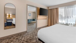 A hotel room with a large bed, a TV mounted on the wall, a mirror, a sofa, and a small table.