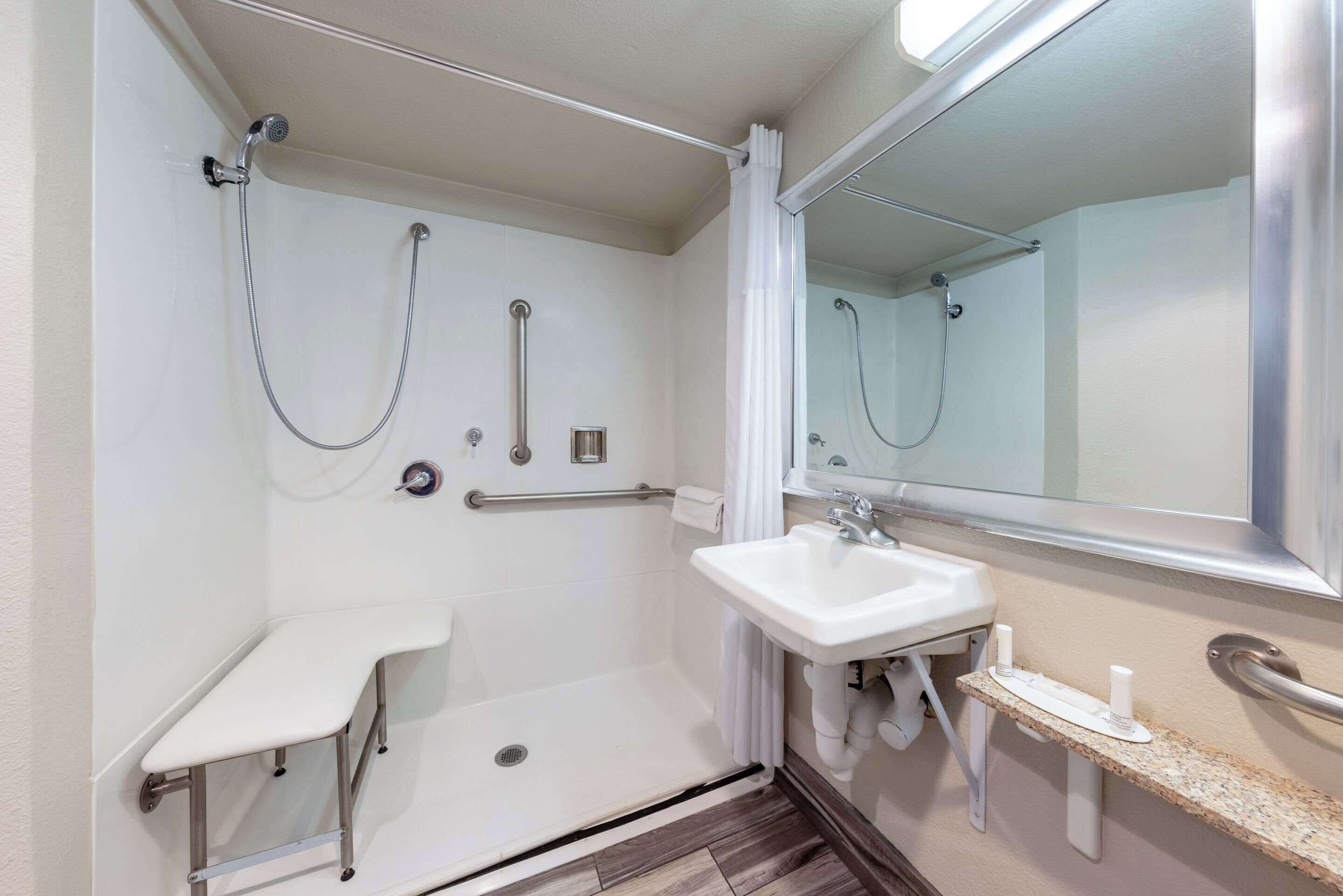 A bathroom with a shower, a sink, a mirror, and a grab bar.