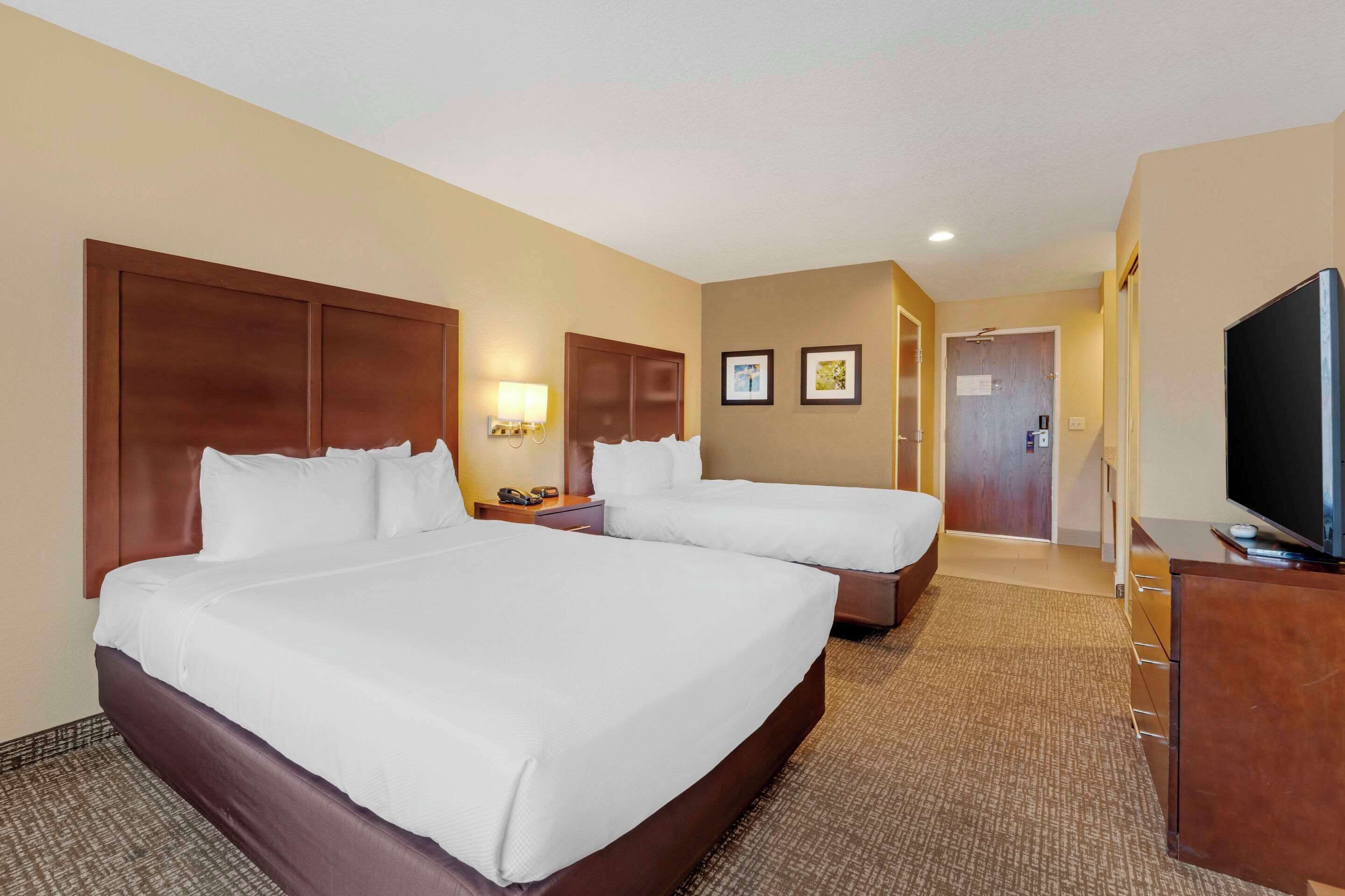 A hotel room with two beds, a TV, a desk, and a lamp.