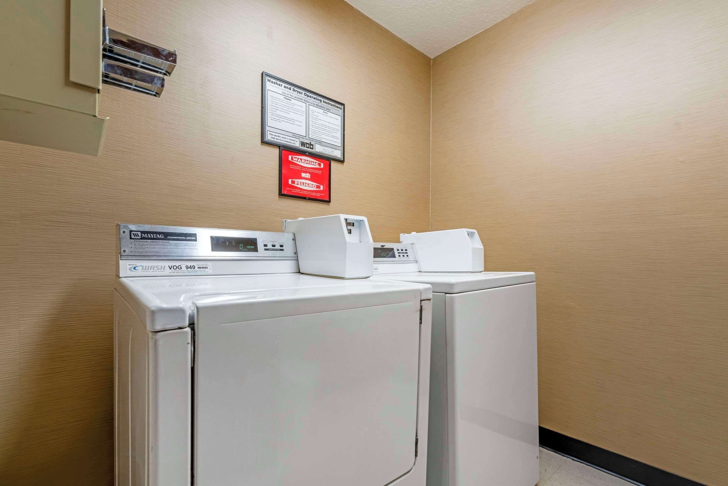 A laundry area with two front-loading washers and dryers, a safety sign, and a wall-mounted instruction sign.