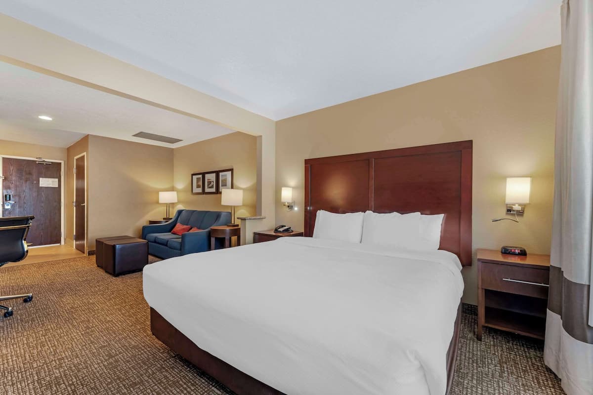 A hotel room with a large bed, a desk with a chair, a sofa, and two bedside tables with lamps.