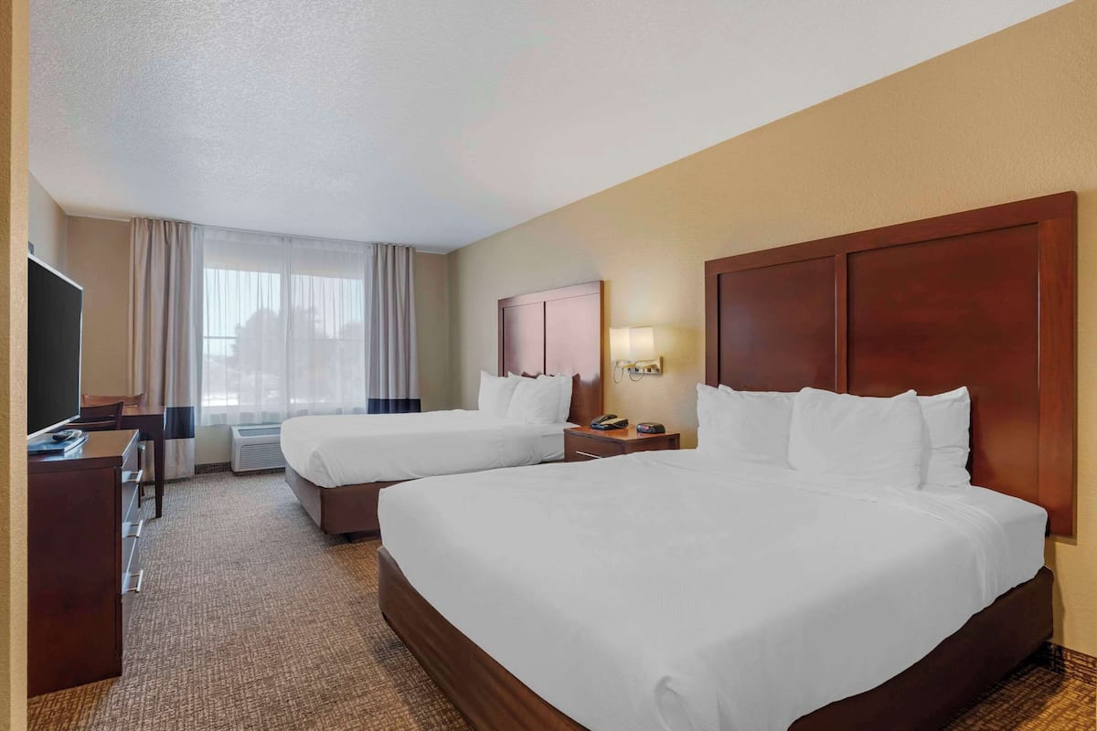 A hotel room with two beds, a desk, a TV, and a window with curtains.