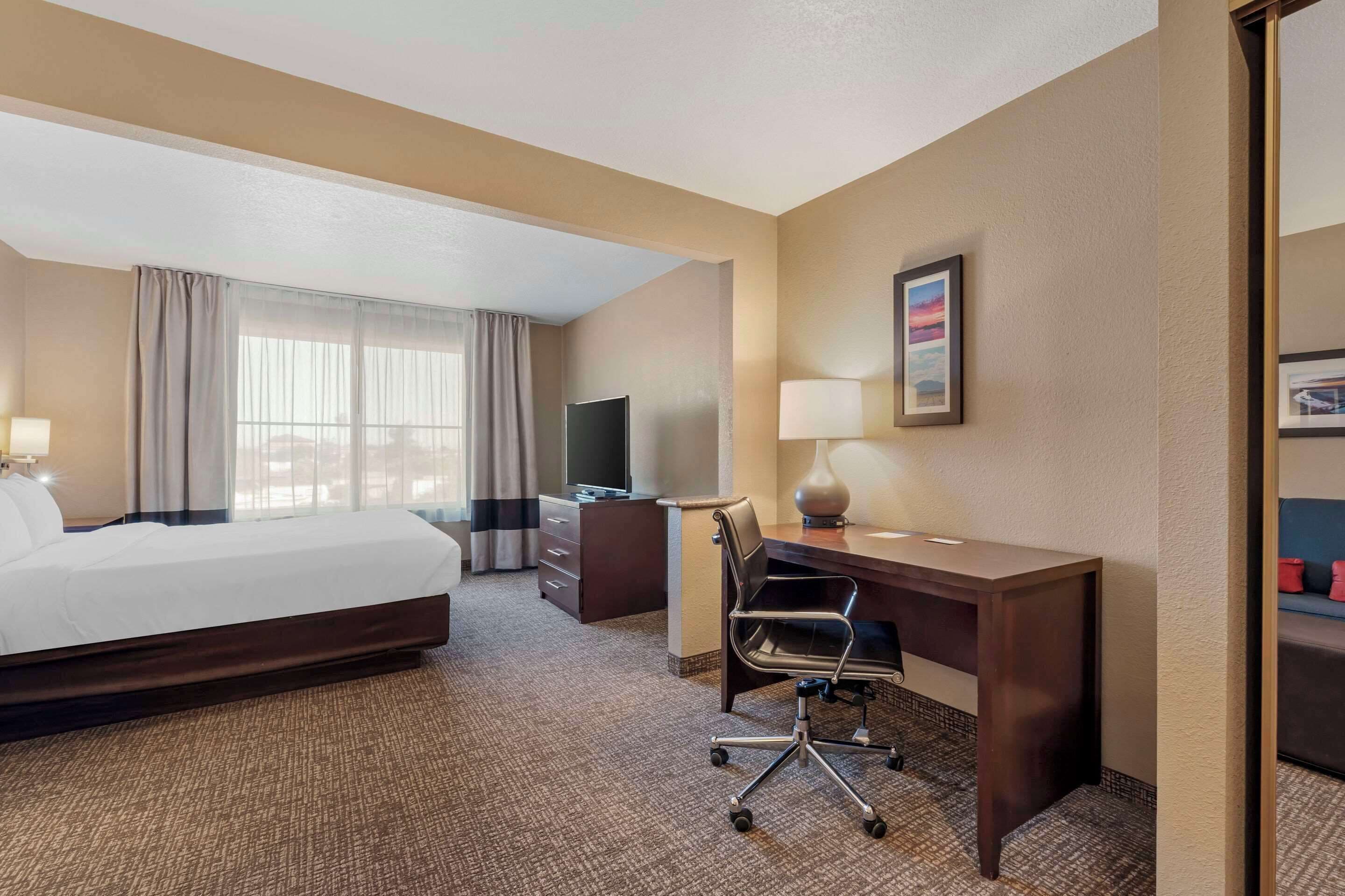 A hotel room with a bed, desk, chair, TV, and a window with curtains.