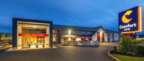A Comfort Inn hotel with a modern design, featuring a prominent sign, outdoor seating area, and a well-lit entrance.