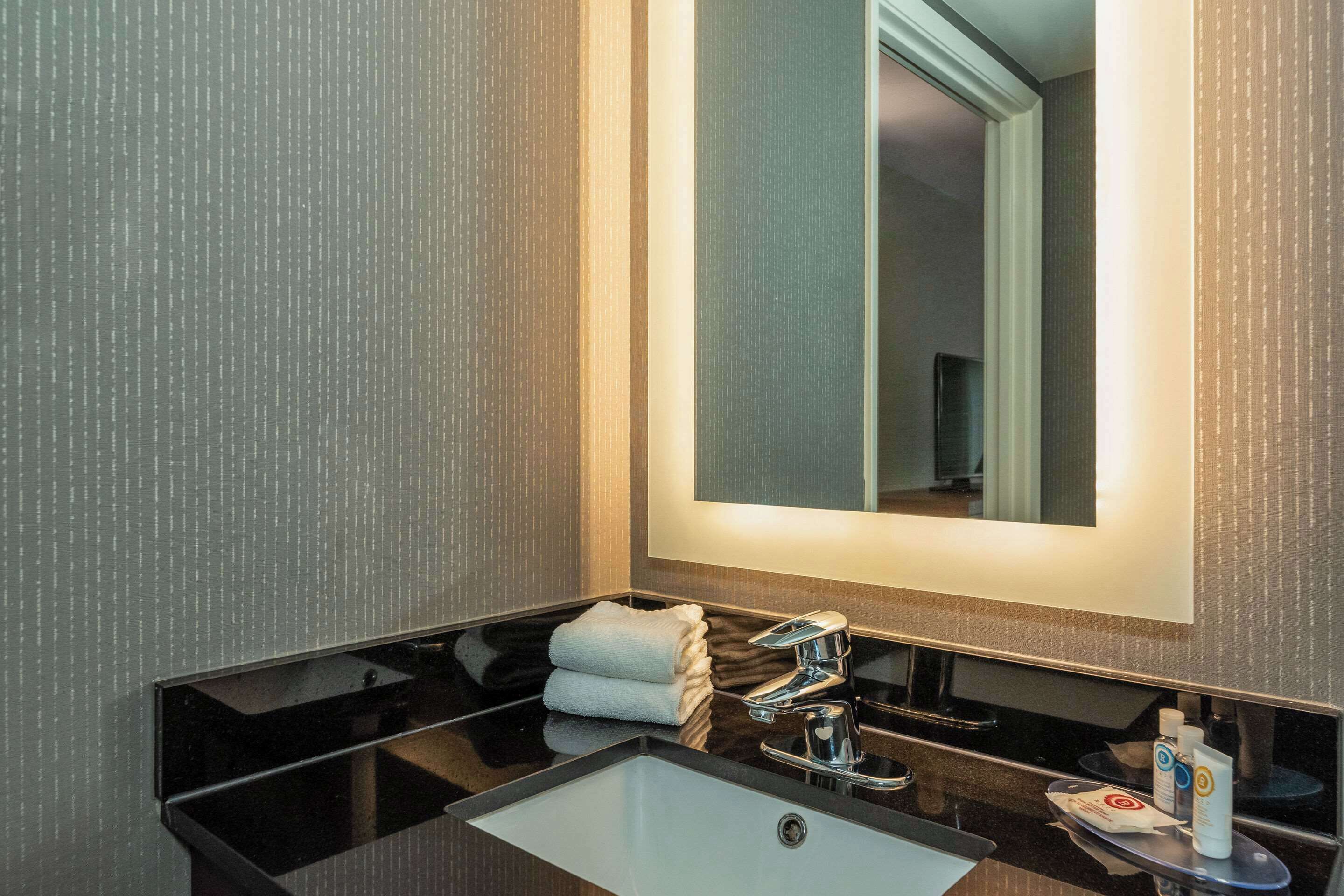Un baño moderno con un lavamanos negro, un espejo y un perchero para toallas.
