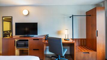 A hotel room with a wooden desk, a flat-screen TV, a microwave, a chair, and a wardrobe.