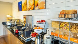 A buffet setup with various food items, a coffee station, and a wall with fruit-themed artwork. - Comfort Inn Charlottetown (Charlottetown)