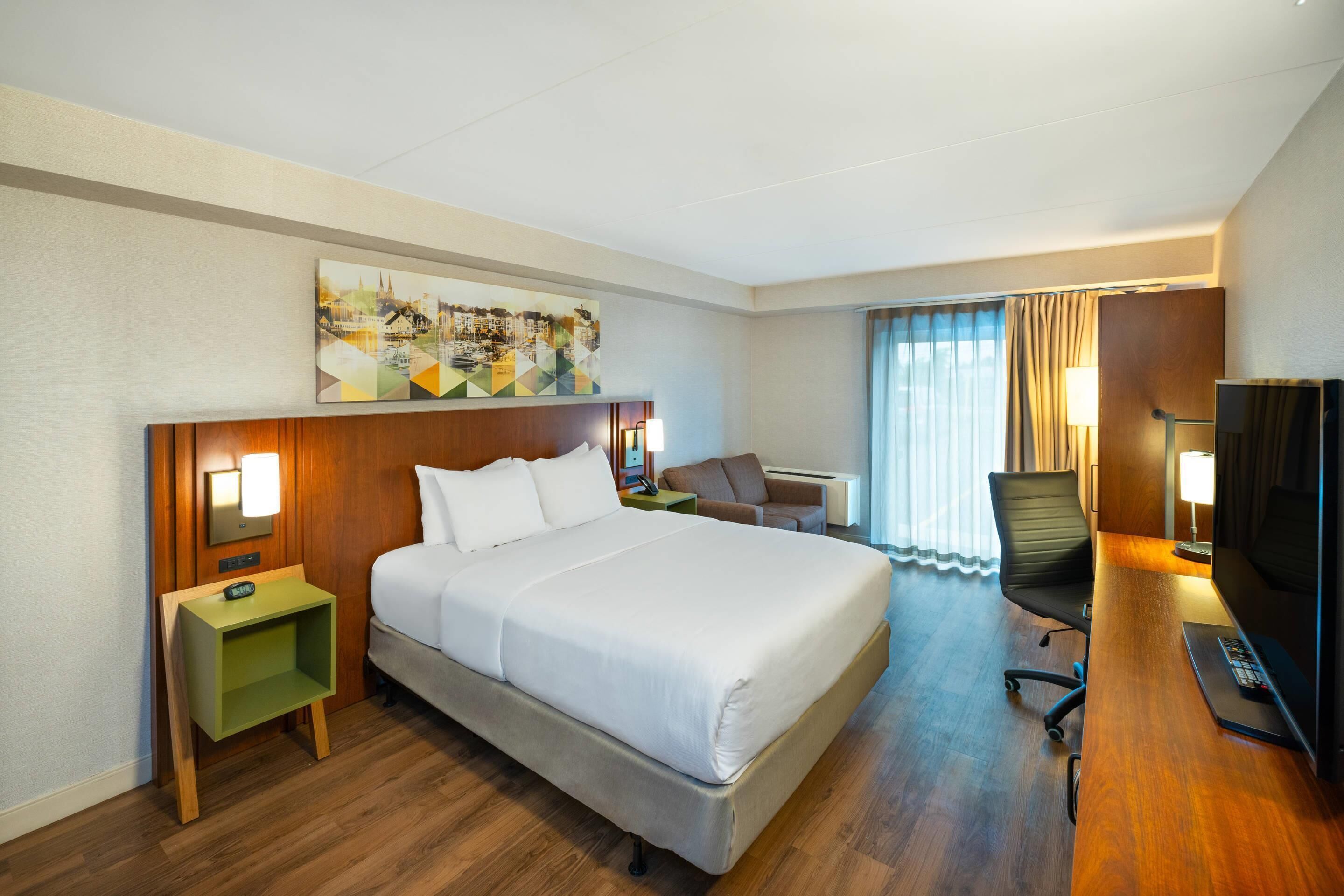Habitación de hotel con una cama grande, un escritorio con silla, un televisor y un cuadro en la pared.