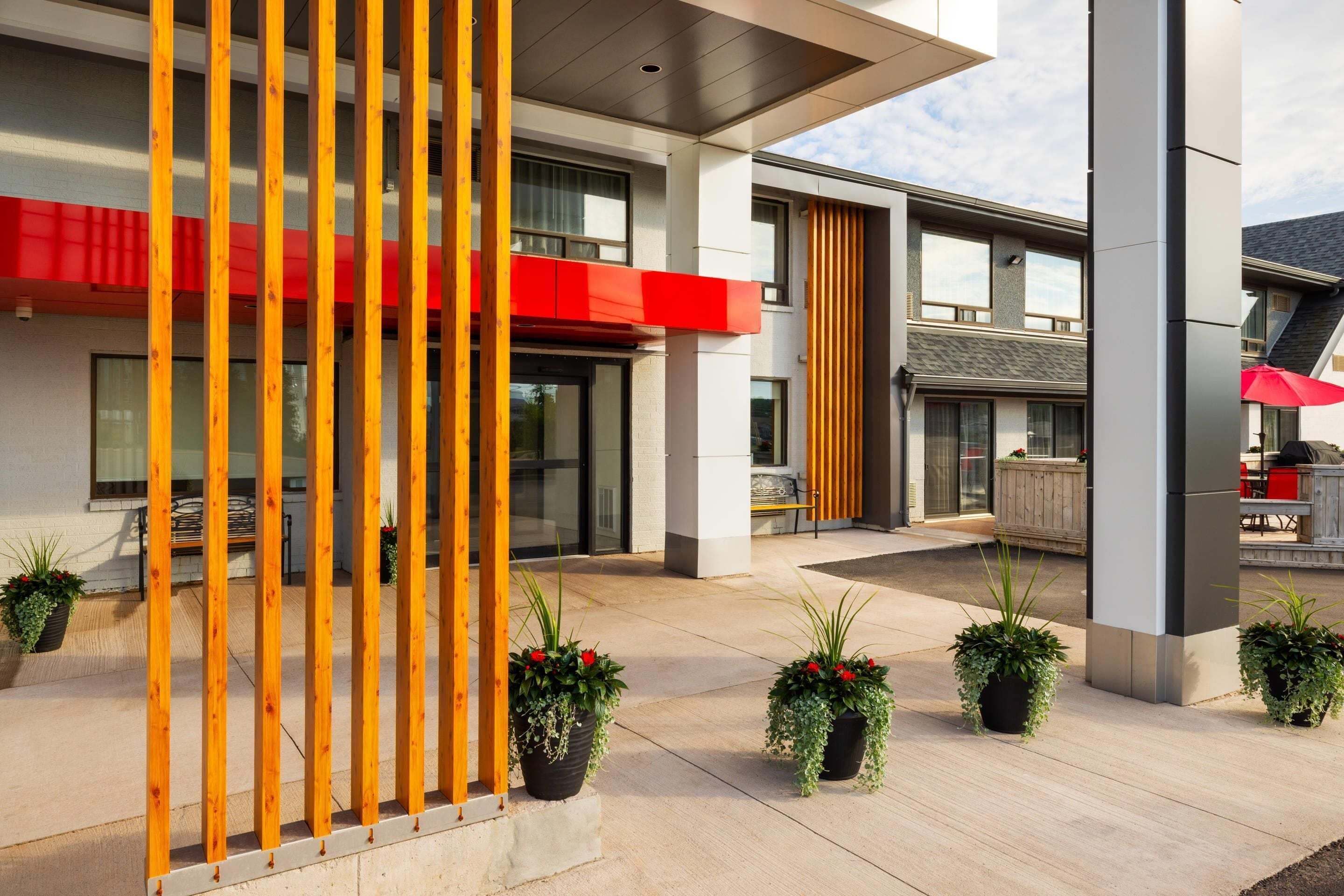Un edificio moderno con un área exterior cubierta, plantas en macetas y un toldo rojo.