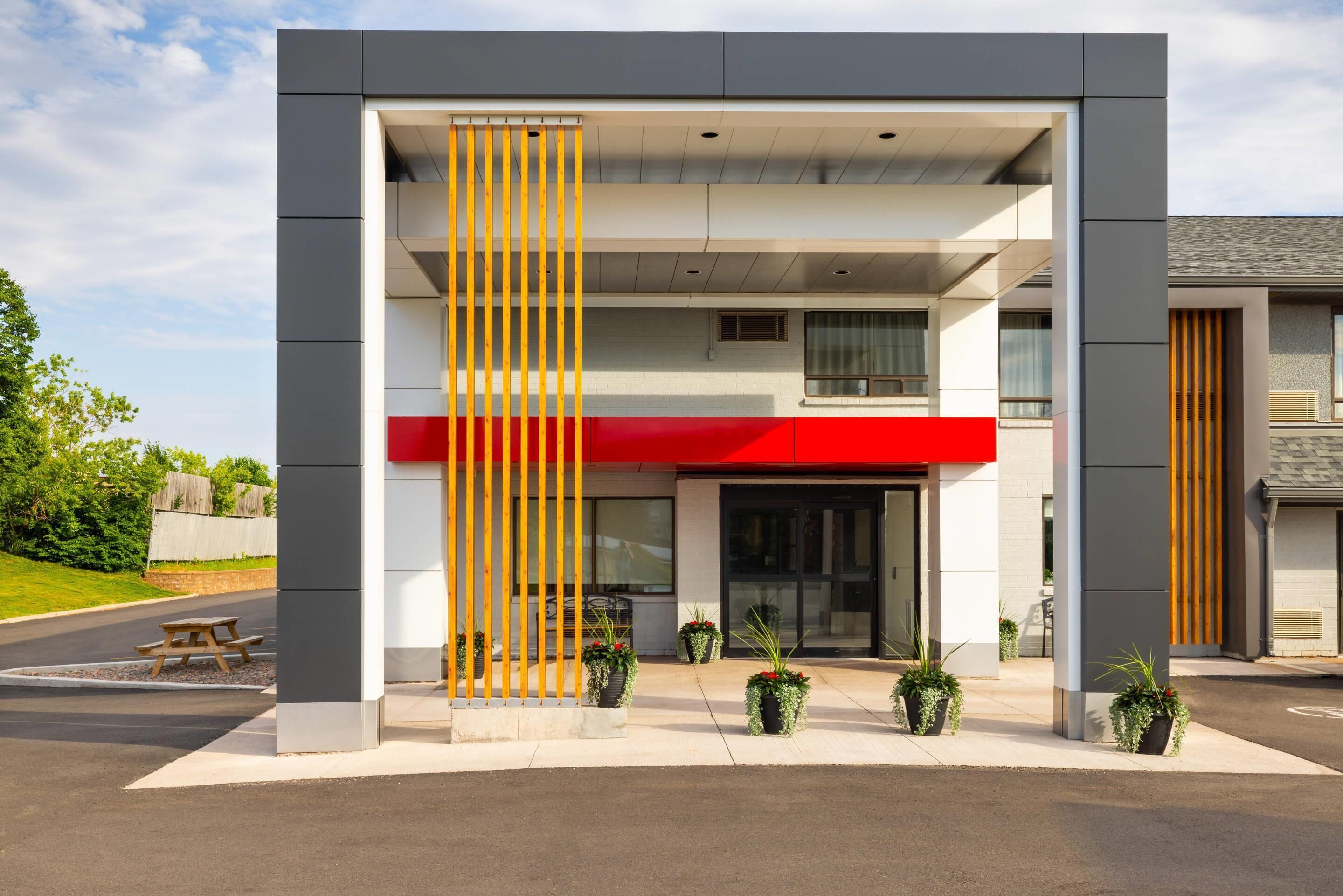 A modern building with a red awning, a vertical wooden slat design, and potted plants in front.