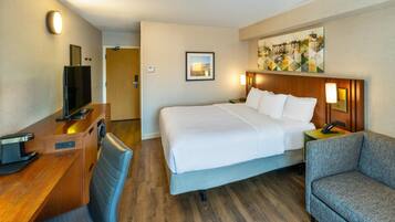 A hotel room with a bed, a desk with a computer, a chair, and a painting on the wall.