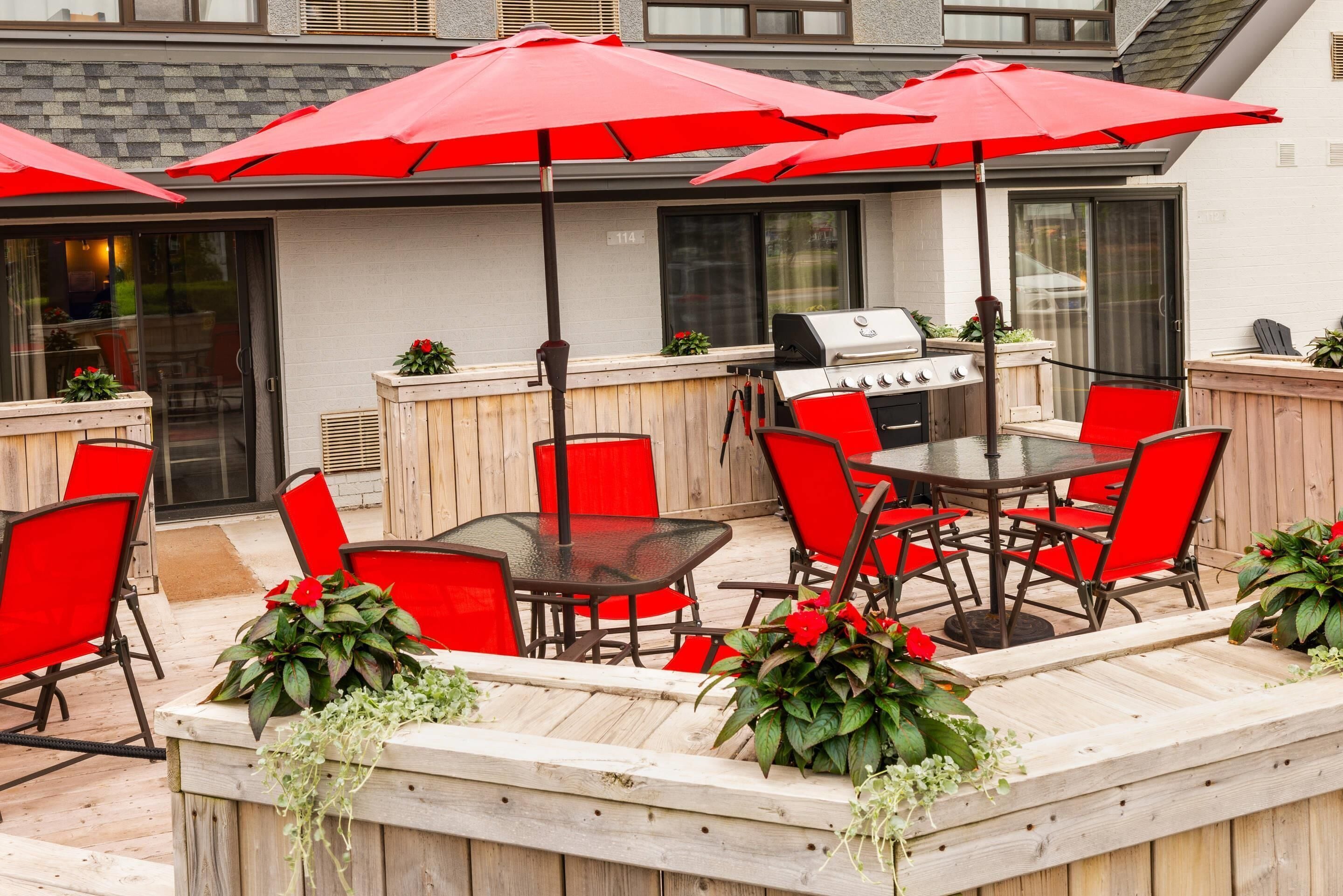 An outdoor patio with a grill, red chairs, and umbrellas.