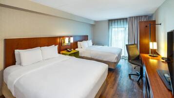 A hotel room with two beds, a desk, a chair, a TV, and a window with curtains.
