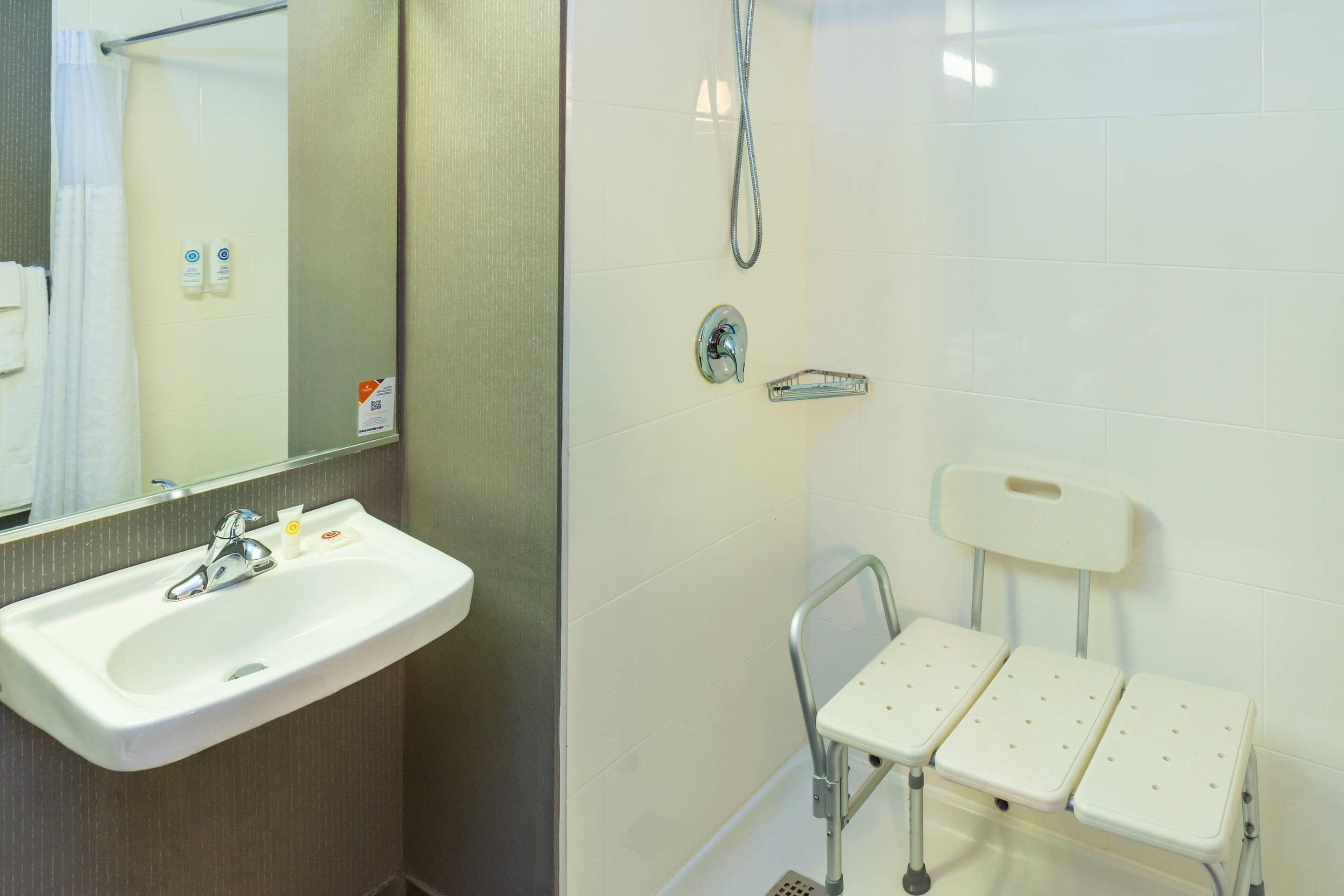 Baño con lavamanos, espejo, ducha y un banco accesible para sillas de ruedas.