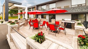 An outdoor patio with red chairs and umbrellas, a barbecue grill, and wooden planters with flowers. - Comfort Inn Charlottetown (Charlottetown)