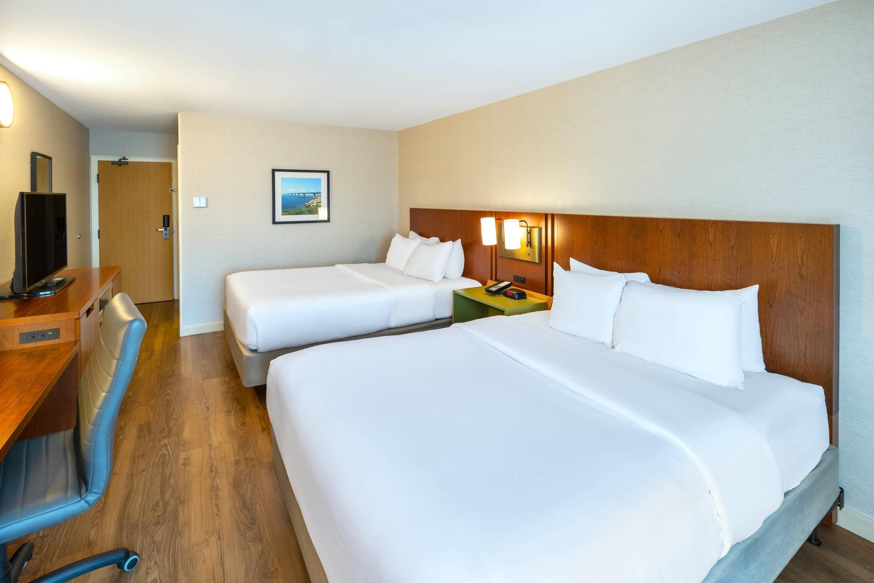 A hotel room with two beds, a desk, a chair, and a television.