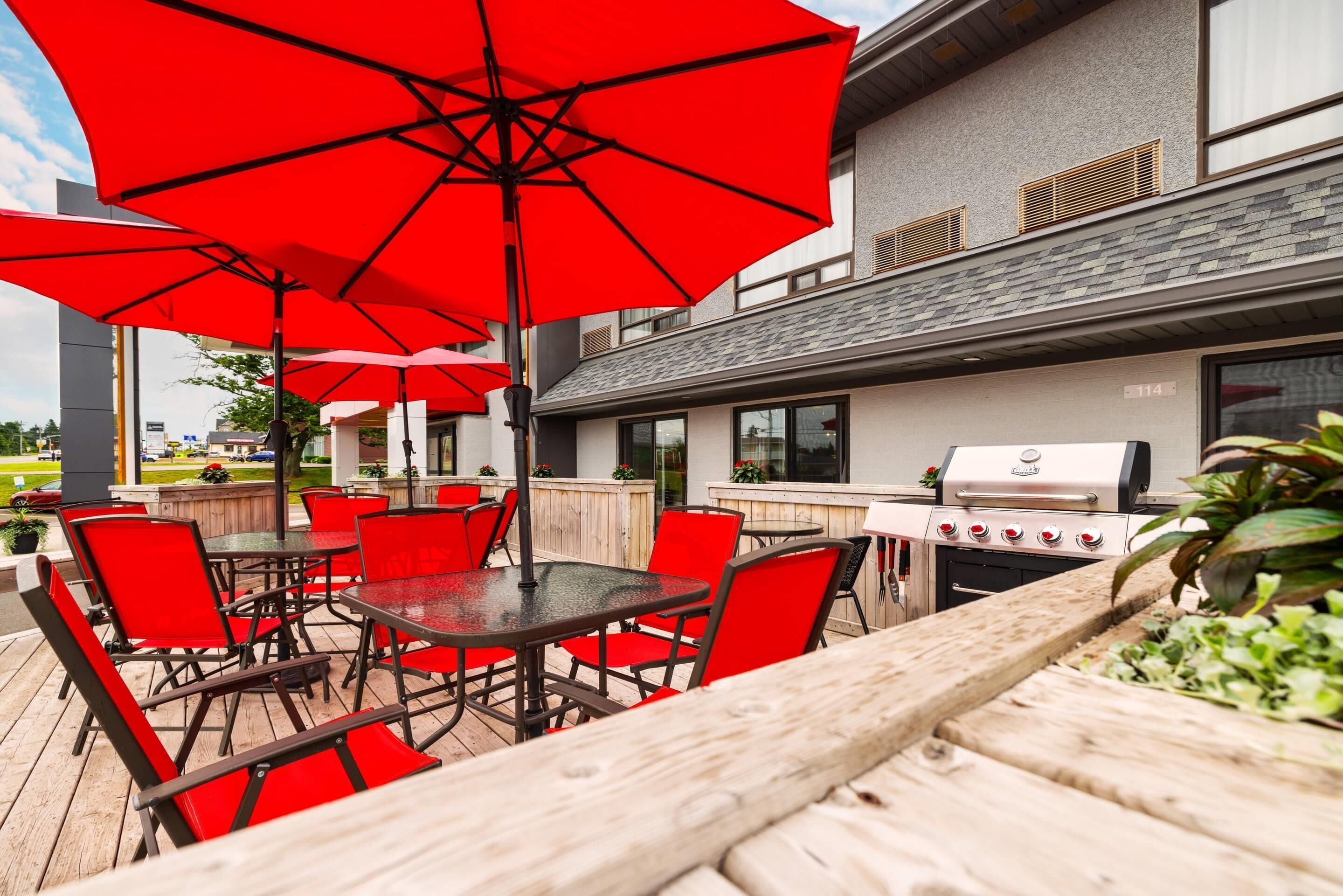 An outdoor patio with red chairs and umbrellas, a grill, and a wooden deck.