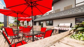 An outdoor patio with red chairs and umbrellas, a grill, and a wooden deck.
