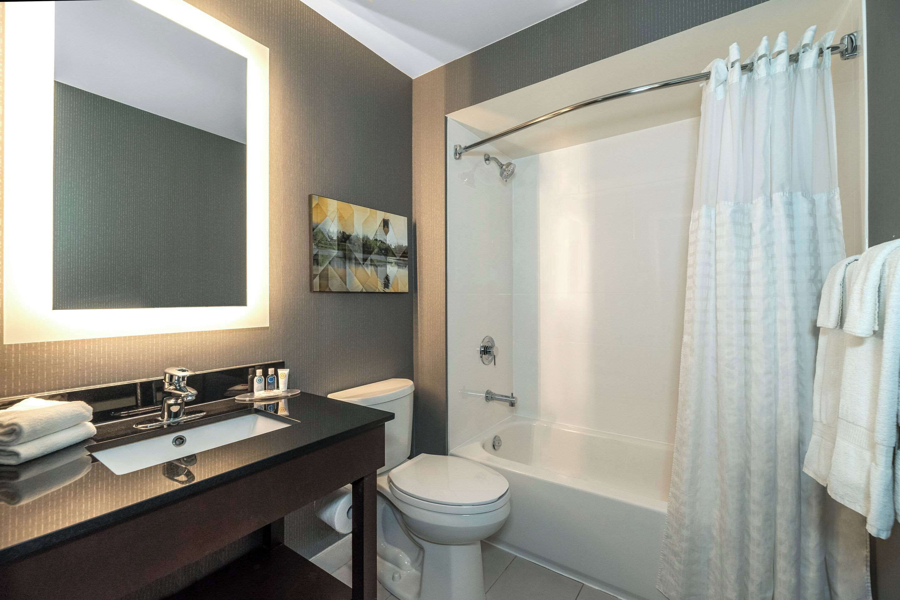 A modern bathroom with a dark vanity, a white toilet, a bathtub, and a shower curtain.