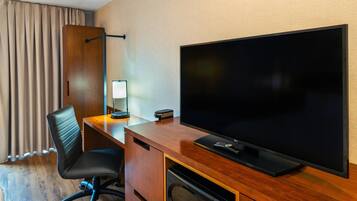 Een hotelkamer met een houten bureau, een grote flatscreen televisie, een zwarte bureaustoel, een lamp en een magnetron.