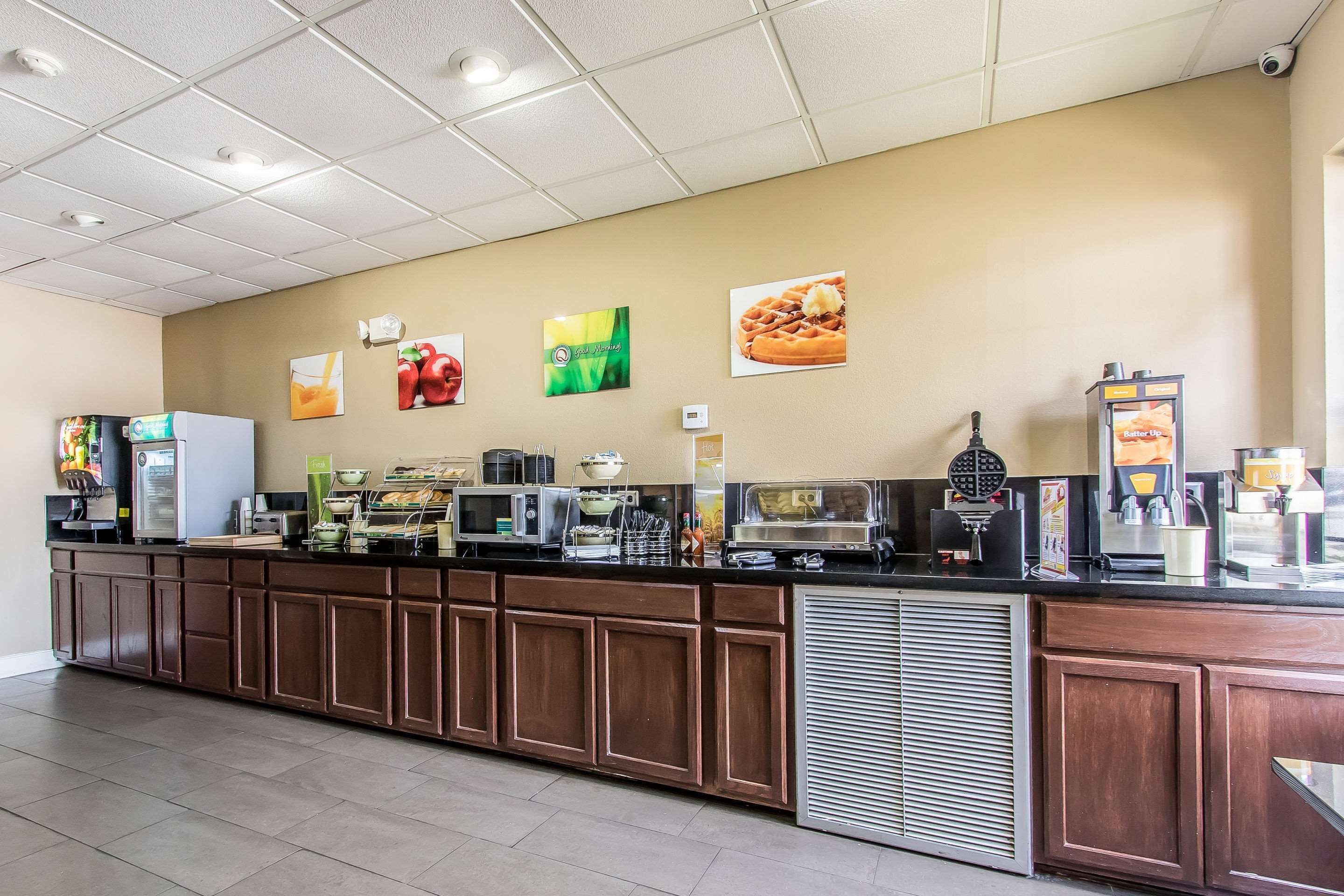 A long counter with various food and drink dispensers, a microwave, and a waffle maker.