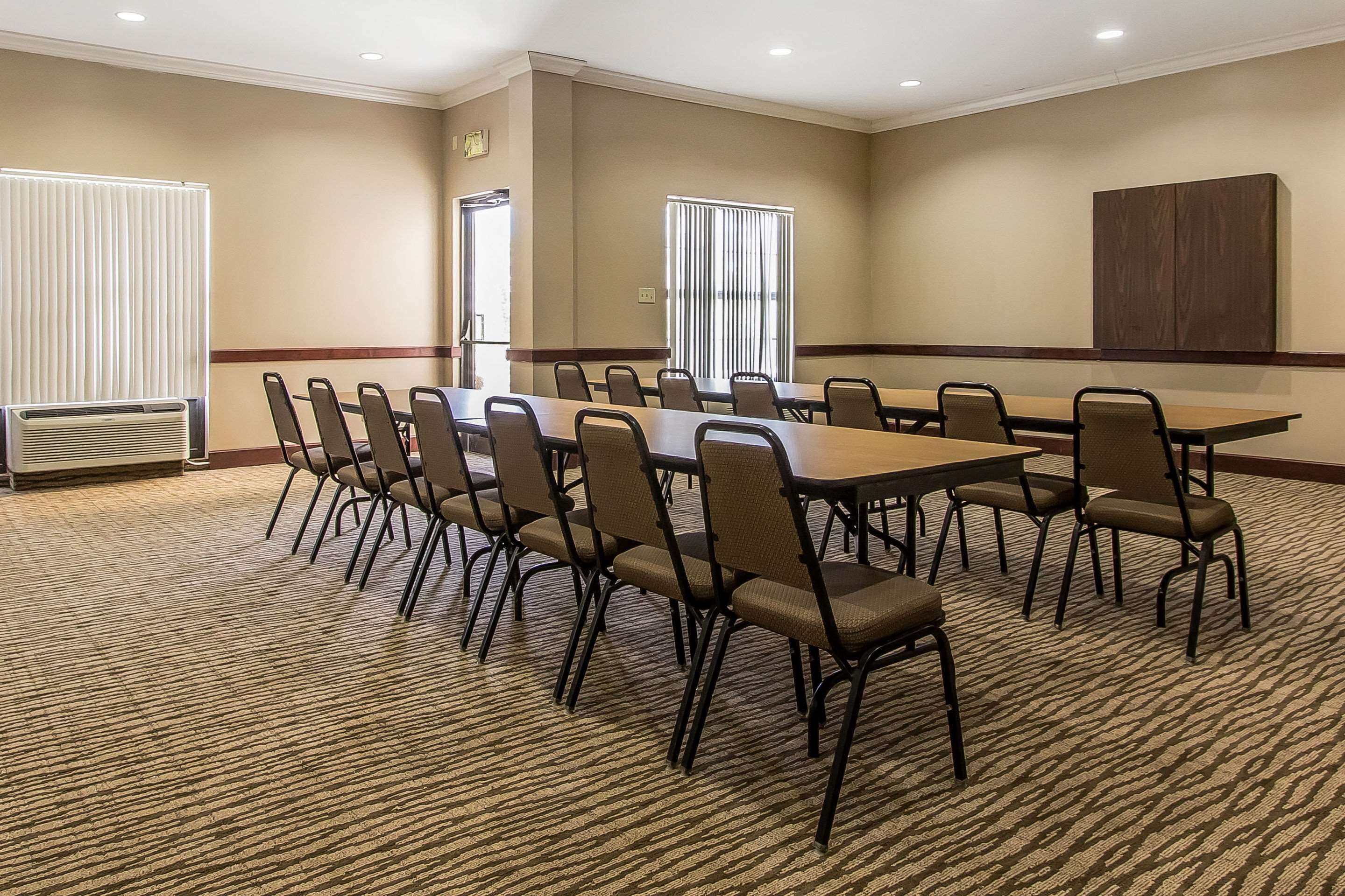 A conference room with a long table and chairs, carpeted floor, and a large window with blinds.
