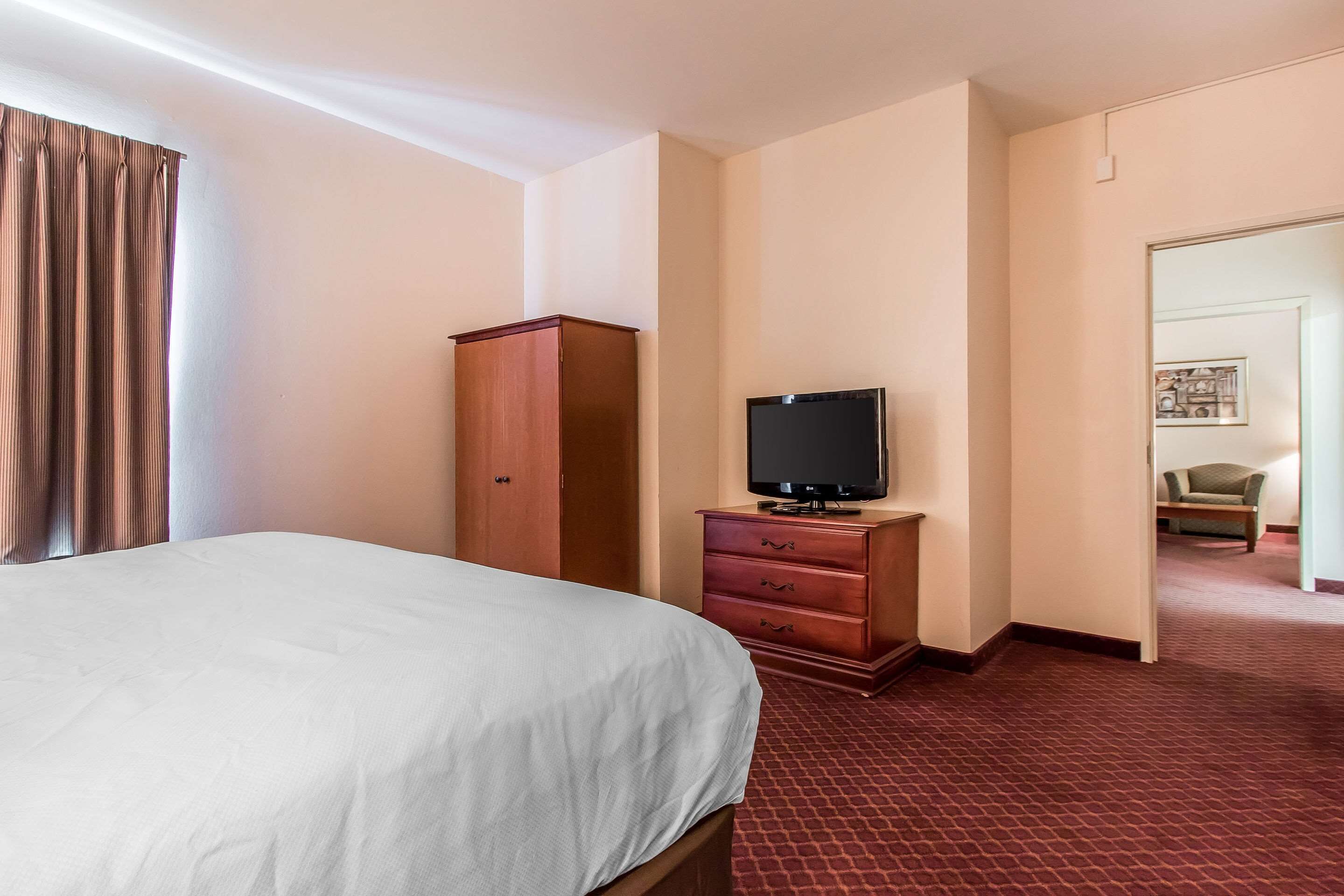 A hotel room with a bed, a wooden dresser, a television, and a door leading to another room.