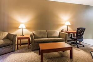 A room with a sofa, two armchairs, a coffee table, a desk, and a chair. There are two lamps on the desk and a phone on the desk.