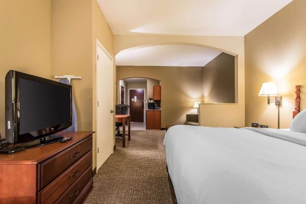 Une chambre d’hôtel avec un lit, un téléviseur posé sur une commode, un bureau et, au fond, une petite cuisine.