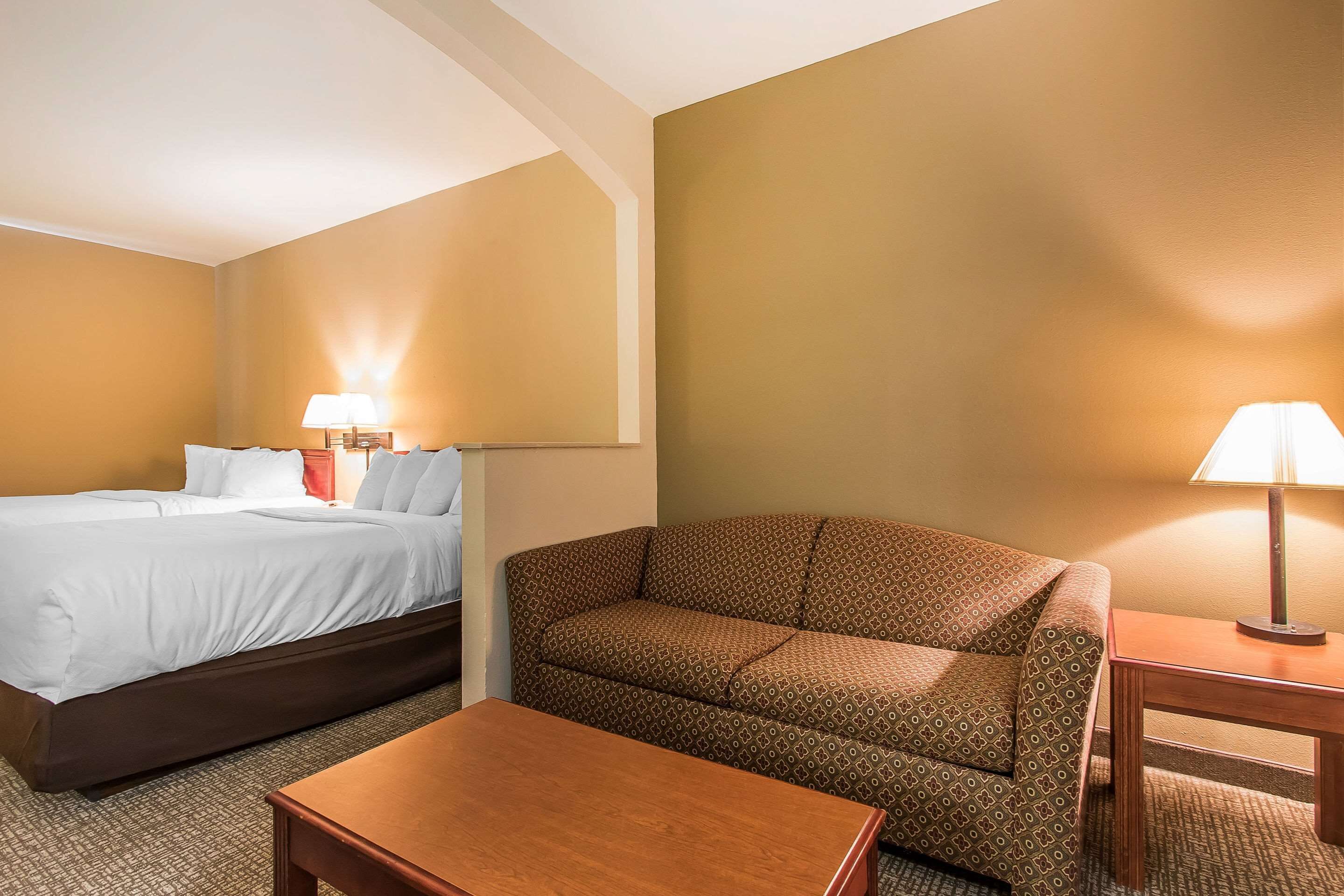 Quarto de hotel com cama, sofá, uma mesinha e duas luminárias.