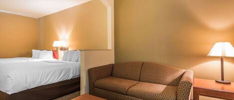 A hotel room with a bed, a sofa, a small table, and two lamps.