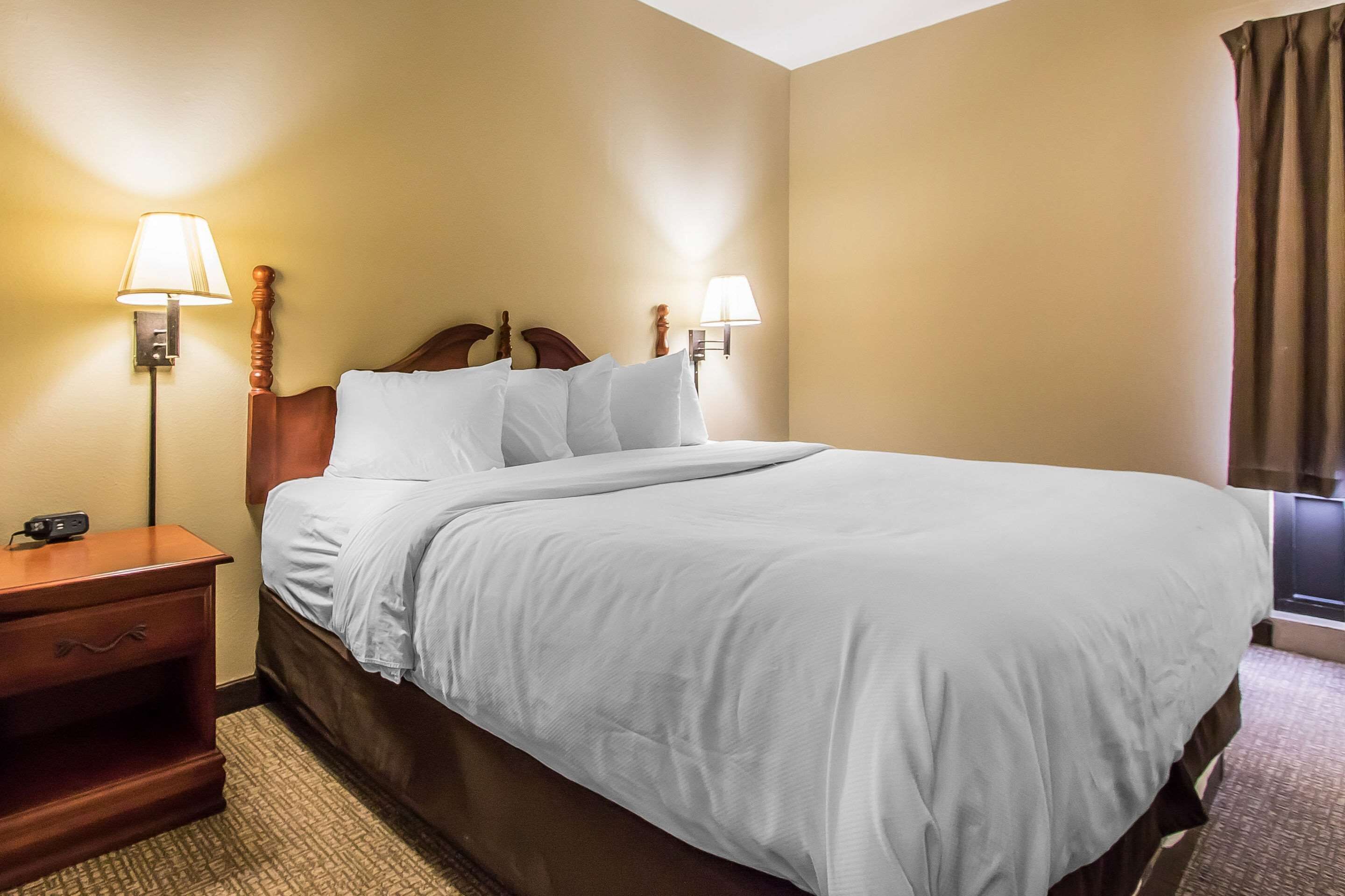 A neatly made bed with white linens in a hotel room. There are two wall-mounted lamps on either side of the bed.