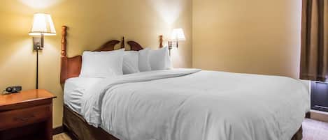 A neatly made bed with white linens in a hotel room. There are two wall-mounted lamps on either side of the bed.