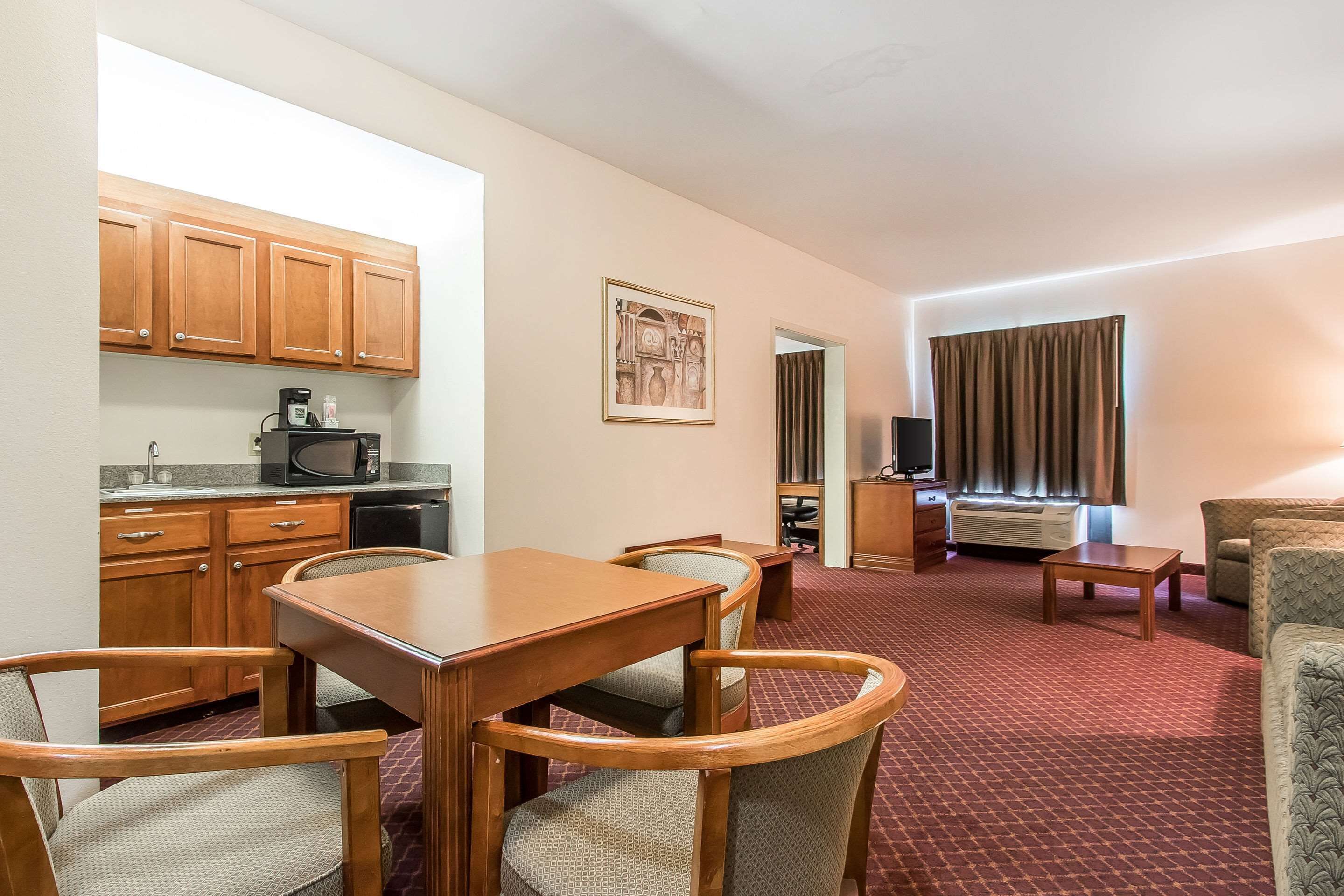 A hotel room with a dining area, kitchenette, and a living area with a sofa and a TV.