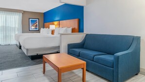 Una habitación de hotel con una cama, un sofá azul, una mesa de madera y un cuadro en la pared.