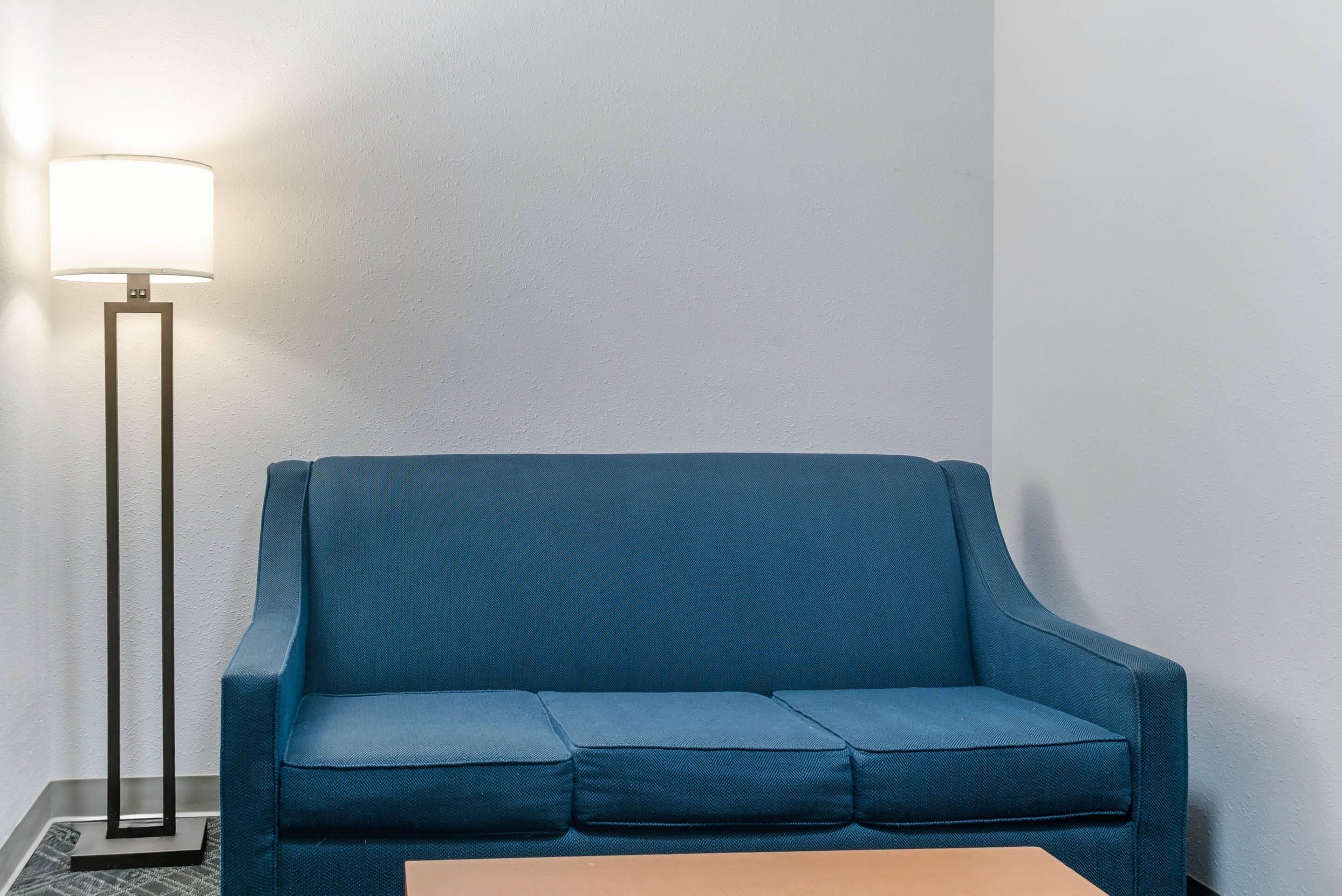 A blue sofa against a plain wall with a floor lamp to the left.