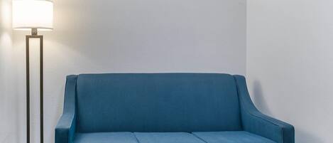 A blue sofa against a plain wall with a floor lamp to the left.