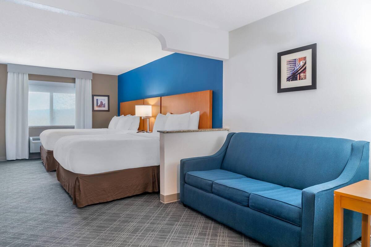 Une chambre d’hôtel avec deux lits, un canapé bleu, une table de chevet avec une lampe et un tableau encadré au mur.